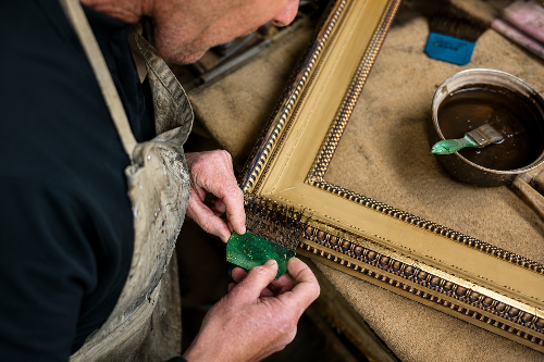 A close-up of a craftsman applying Gold leaf to the corner of an ornate gold picture frame on a workbench, Gold leaf is applied to the surface using a brushed on wet gelatine "size" which adheres it to the surface. Gelatine is supplied by MM Ingredients