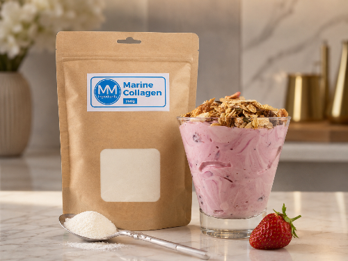 A pouch of MM Ingredients marine collagen powder next to a glass containing a strawberry smoothie with collagen powder in topped by granola on a marble worktop