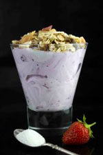 A glass of strawberry yogurt with granola on a black background and in the foreground a spoon of MM Ingredients supplied collagen powder and a strawberry