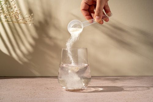 Collagen powder being poured into a glass of liquid on a clean surface